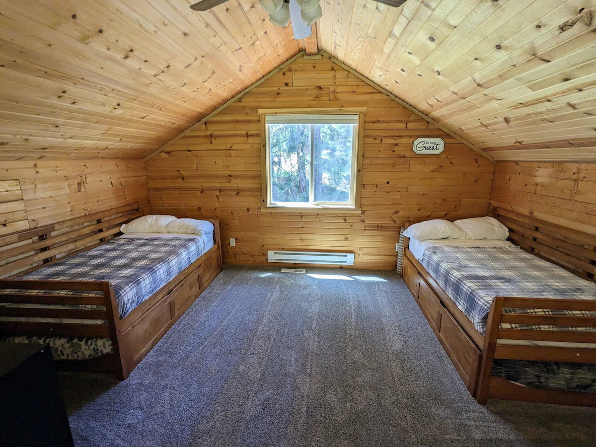 Loft bedroom with twin beds and pine-paneled angled ceiling