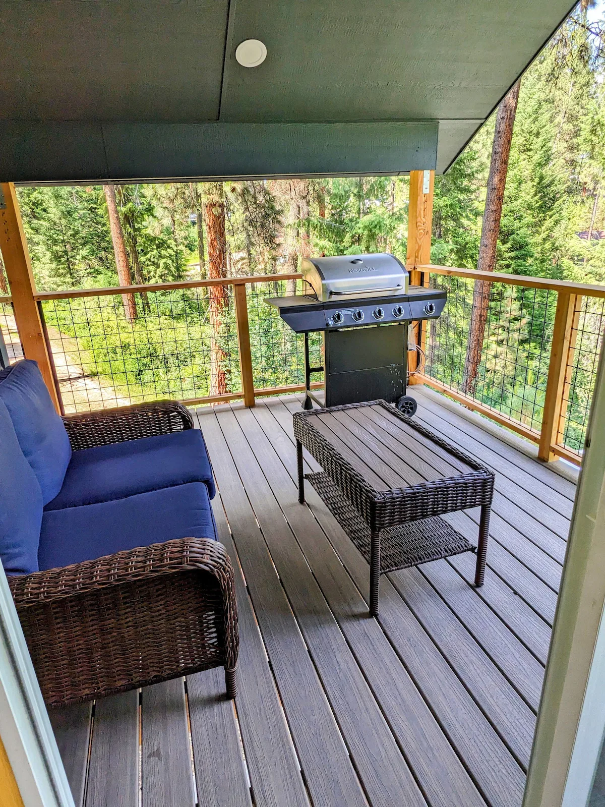 Covered deck with patio furniture, gas grill, and forest view